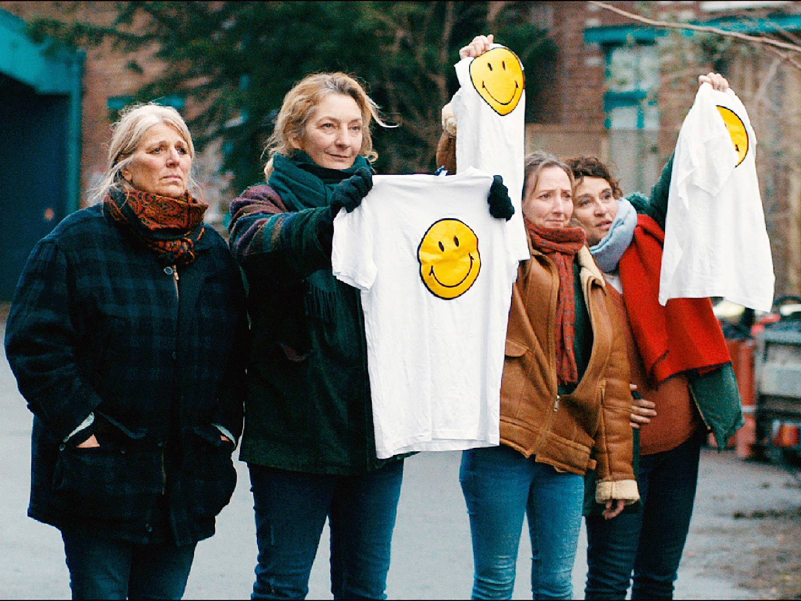 Auf dem Foto zu sehen sind vier Frauen in warmen Jacken. Drei von ihnen halten T-Shirts in die Höhe, auf denen ein lächelnder Smiley zu sehen ist.